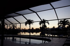 Una piscina interior con vistas despejadas a palmeras y al atardecer.