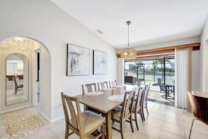 A dining area with a large table, chairs, and a view of a body of water through large windows. - Western Sunsets-Heated Pool-Dock-Fresh Water Canal (Cape Coral)