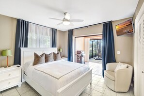 Une chambre à coucher avec un lit, une table de chevet, une lampe, un ventilateur de plafond et une vue sur l’extérieur.