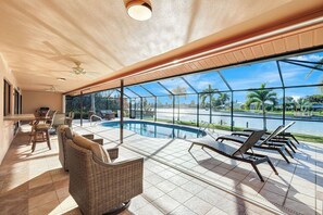 A spacious indoor pool area with a view of a body of water, a ceiling fan, and a seating area with chairs and a sofa. - Western Sunsets-Heated Pool-Dock-Fresh Water Canal (Cape Coral)