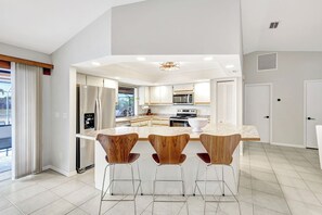 A modern kitchen with a central island, stainless steel appliances, and wooden bar stools. - Western Sunsets-Heated Pool-Dock-Fresh Water Canal (Cape Coral)