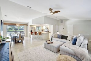 A spacious living area with a large sofa, a dining table, and a kitchen in the background. - Western Sunsets-Heated Pool-Dock-Fresh Water Canal (Cape Coral)