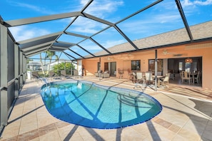 A swimming pool with a glass ceiling, surrounded by lounge chairs and a dining area. - Western Sunsets-Heated Pool-Dock-Fresh Water Canal (Cape Coral)