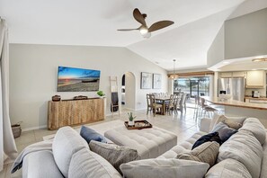 A spacious living room with a large sofa set, a dining area with a table and chairs, a kitchen area, and a ceiling fan. - Western Sunsets-Heated Pool-Dock-Fresh Water Canal (Cape Coral)