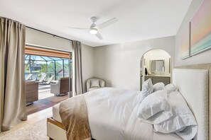 Habitación de hotel con cama, ventilador de techo, ventana grande y balcón con sillas.