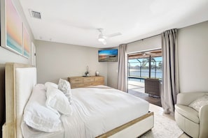 Une chambre à coucher comprenant un lit, une commode, un téléviseur et donnant sur un plan d’eau.
