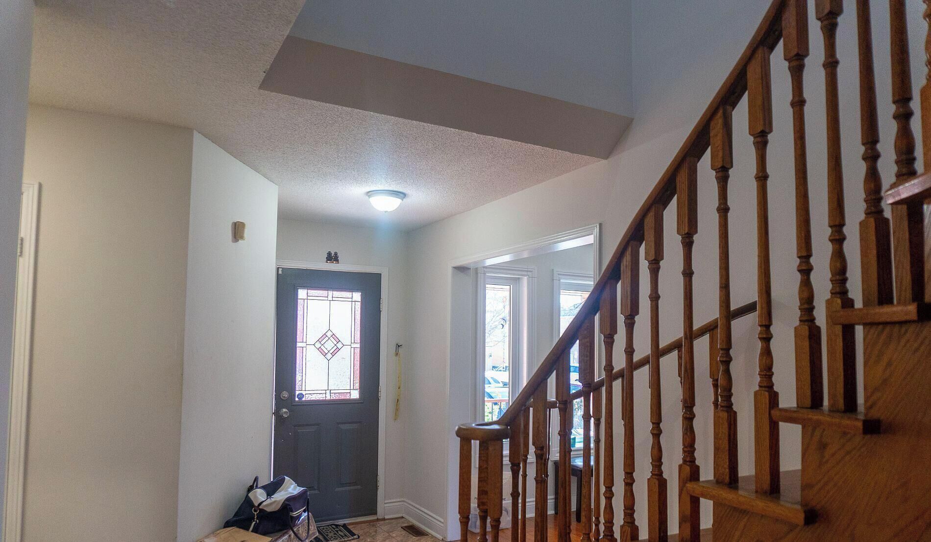A hallway with a wooden staircase, a door with a stained glass window, and a ceiling light.