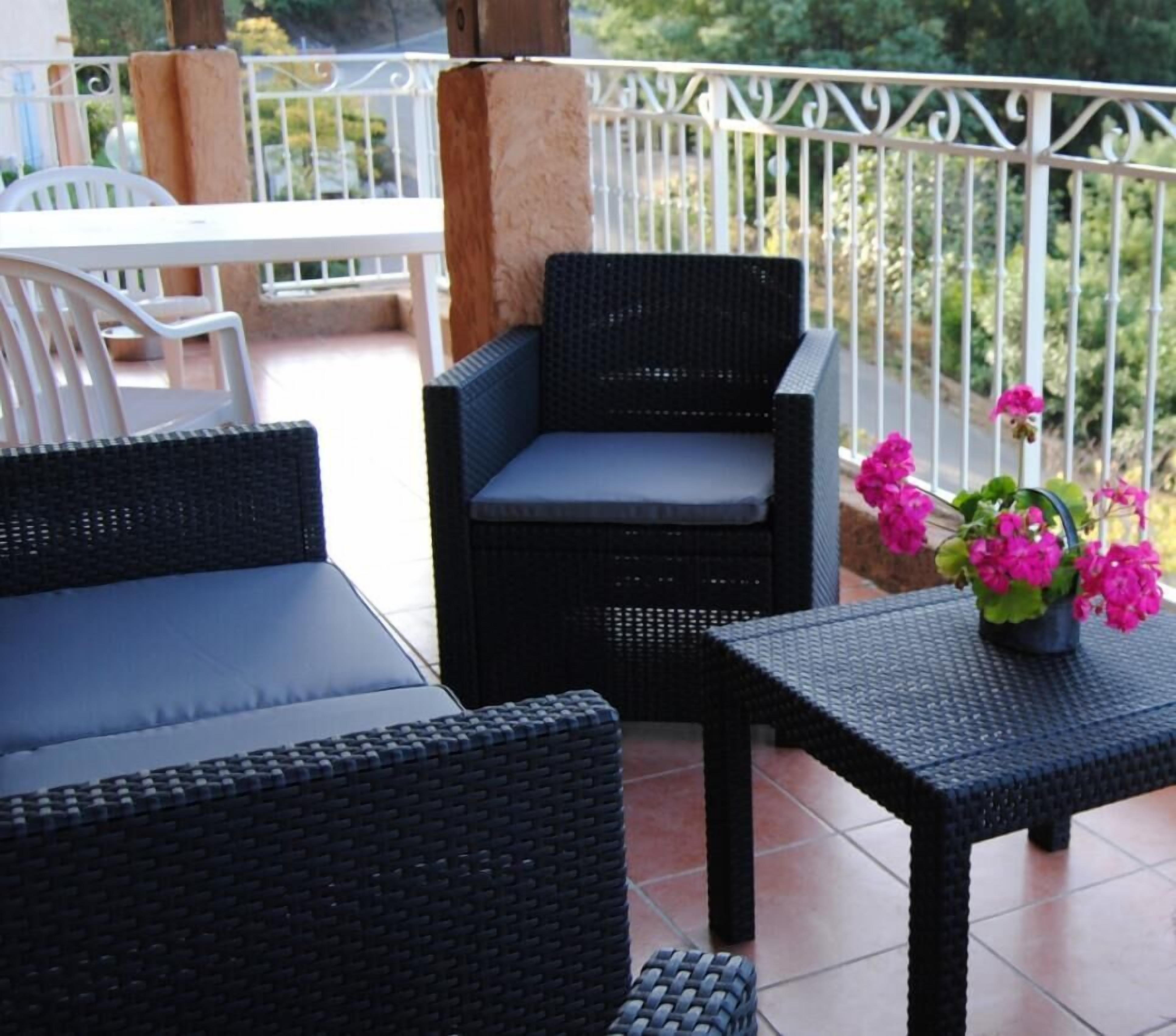 A balcony with wicker furniture, a table with flowers, and a white railing.