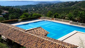 A swimming pool with a tiled deck, surrounded by greenery and a view of a distant coastline. - Cornazur: Ocean View, Pool, and Reversible Air Conditioning (ROQUEBRUNE SUR ARGENS)
