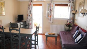 A room with a dining table, chairs, a sofa, a television, and a window with curtains. - Cornazur: Ocean View, Pool, and Reversible Air Conditioning (ROQUEBRUNE SUR ARGENS)