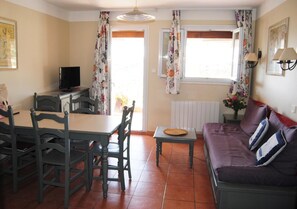 Ein Zimmer mit Esstisch, Stühlen, einer Couch, einem Fernseher und einem fenster mit Vorhängen.
