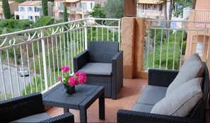 Un balcon agrémenté de meubles en osier, une petite table décorée de fleurs et une vue sur les bâtiments environnants.