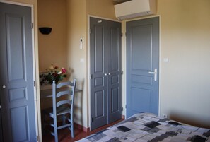 A bedroom with two doors, a bed with a quilt, a chair, and a wall-mounted air conditioner. - Cornazur: Ocean View, Pool, and Reversible Air Conditioning (ROQUEBRUNE SUR ARGENS)