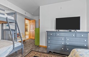 Ein Schlafzimmer mit Etagenbett, einem Schminktisch, einem Fernseher und einer Tür zu einem anderen Raum.
