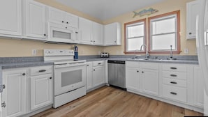 A kitchen with white cabinets, a microwave, stove, dishwasher, and a window with a fish decoration. - SALTED SHORES OBX formerlyPLAYING HOOKY, 5bed,Wild Horses,Pool,Hot Tub,4x4 Beach (Corolla)