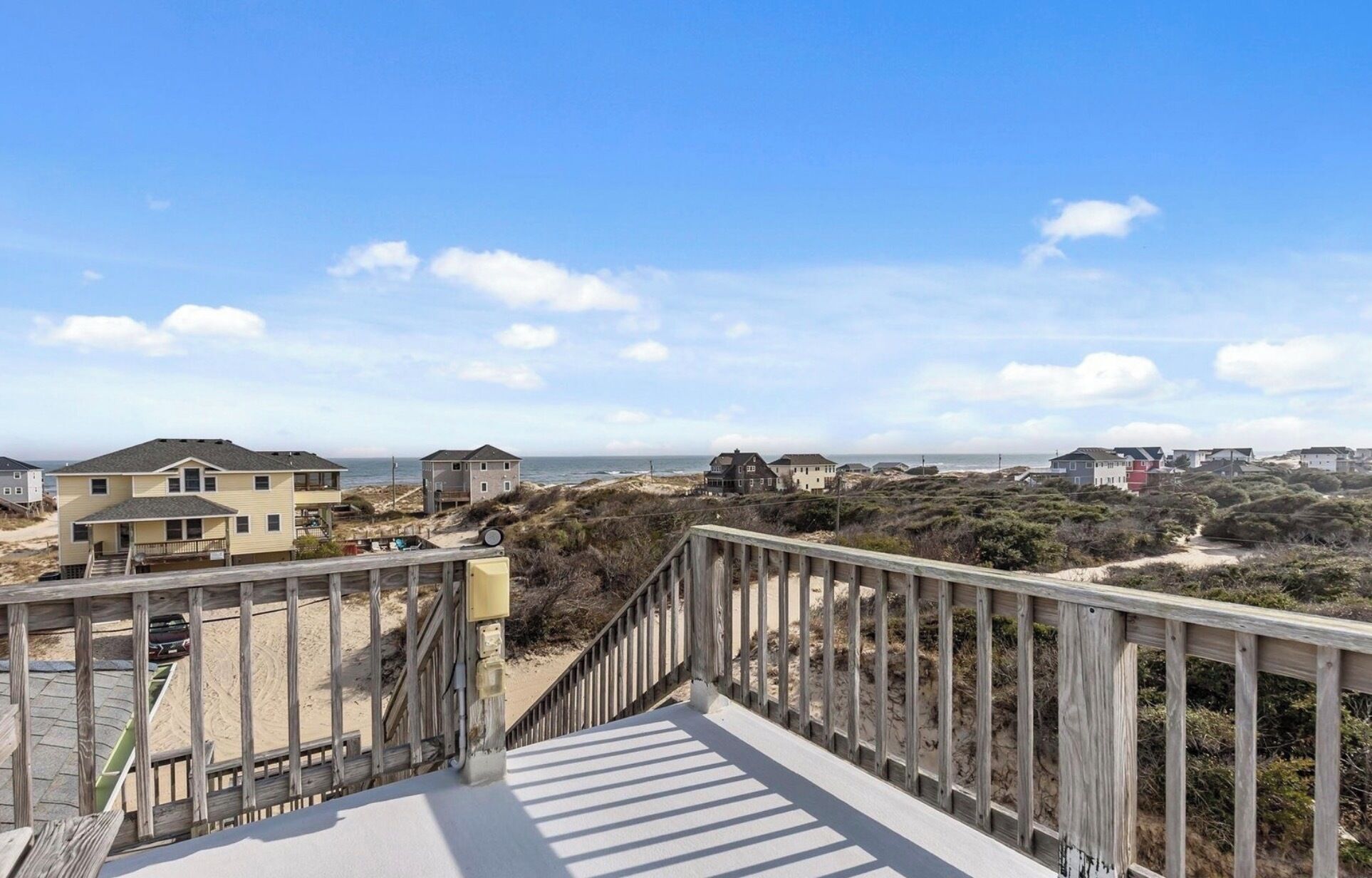 A wooden boardwalk leading to beach houses with a clear view of the ocean.