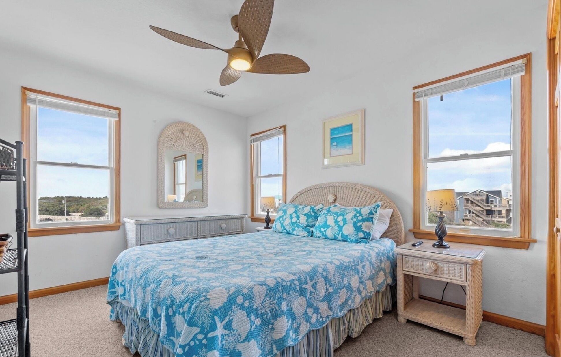 A bedroom with a bed, a nightstand, a ceiling fan, and large windows.