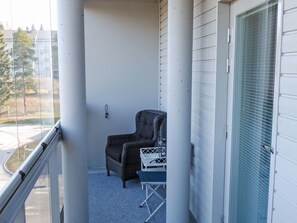 Ein Balkon mit einem Korbstuhl, einem kleinen Tisch, einer weißen Tür und Blick auf die Straße und Bäume.