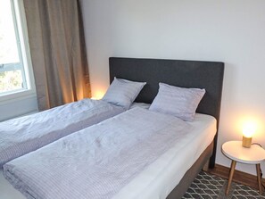A double bed with two pillows, a bedside table with a lamp, and a window with curtains. - Rovaniemi City by Interhome (Rovaniemi)