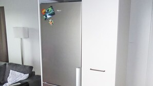 Una cocina moderna con un refrigerador de acero inoxidable, un sofá gris oscuro y una pared blanca.