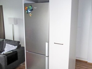 Eine moderne Küche mit einem Edelstahl-Kühlschrank, einem dunkelgrauen Sofa und einer weißen Wand.