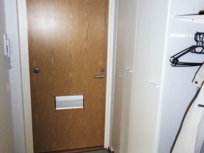Eine Holztür mit Briefschlitz, eine weiße Wand und ein Kleiderhaken mit Kleiderbügeln.