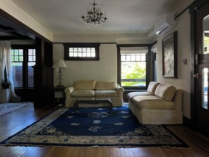 A living room with two sofas, a chandelier, and a large window with curtains.