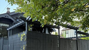 Asuinrakennus, jossa on puinen aita, katettu kuisti ja kasveilla koristeltu puutarha.