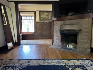 A room with a fireplace, wooden flooring, a rug, and a large window. - Charming 2 bed Craftsman in Upper Fremont, close to everything w/ private garden (Seattle)