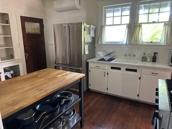 A kitchen with a wooden table, stainless steel appliances, and a window with curtains.