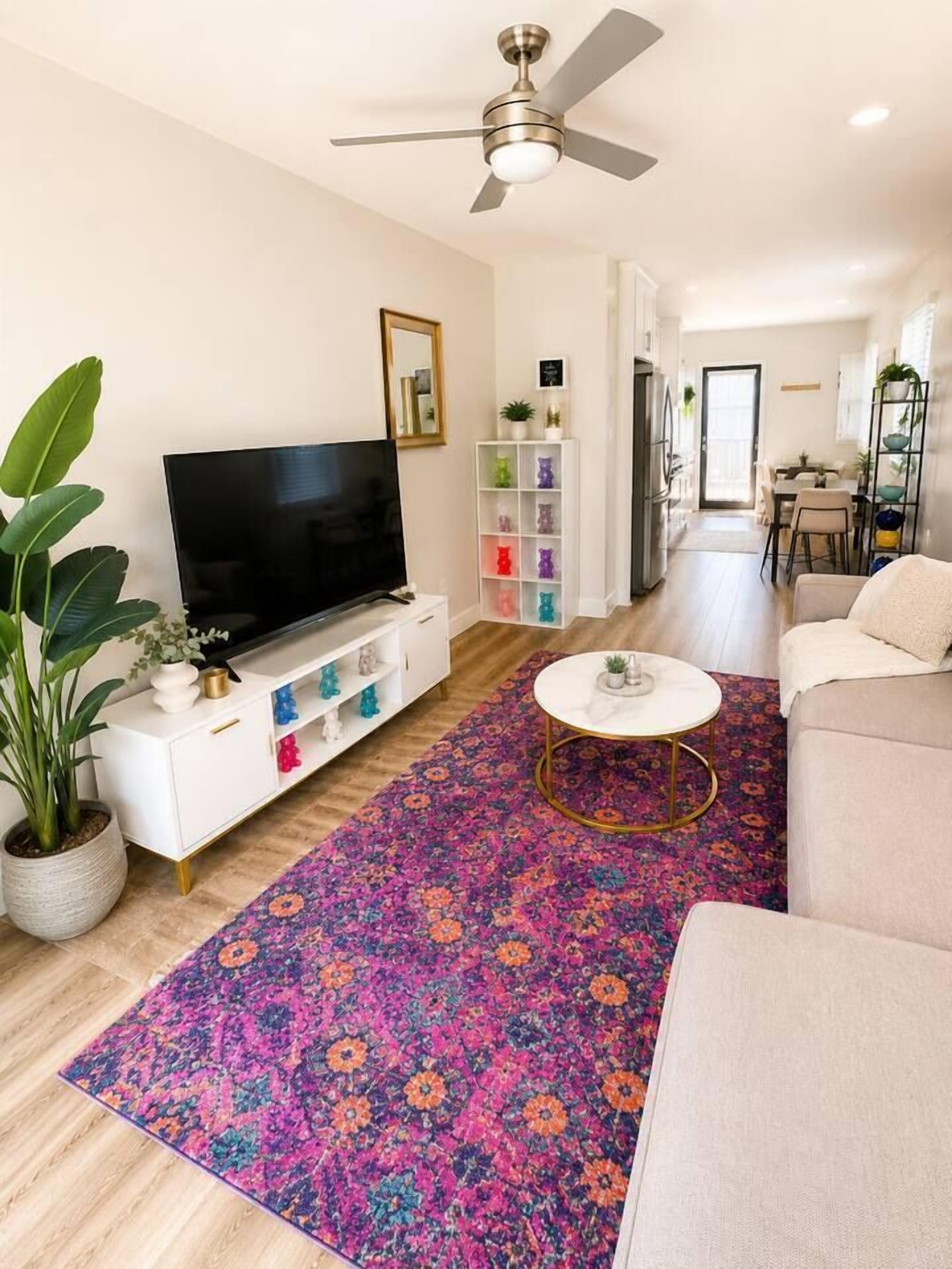 Un salon moderne avec un téléviseur à écran plat, un ventilateur de plafond, un tapis coloré et un canapé blanc.