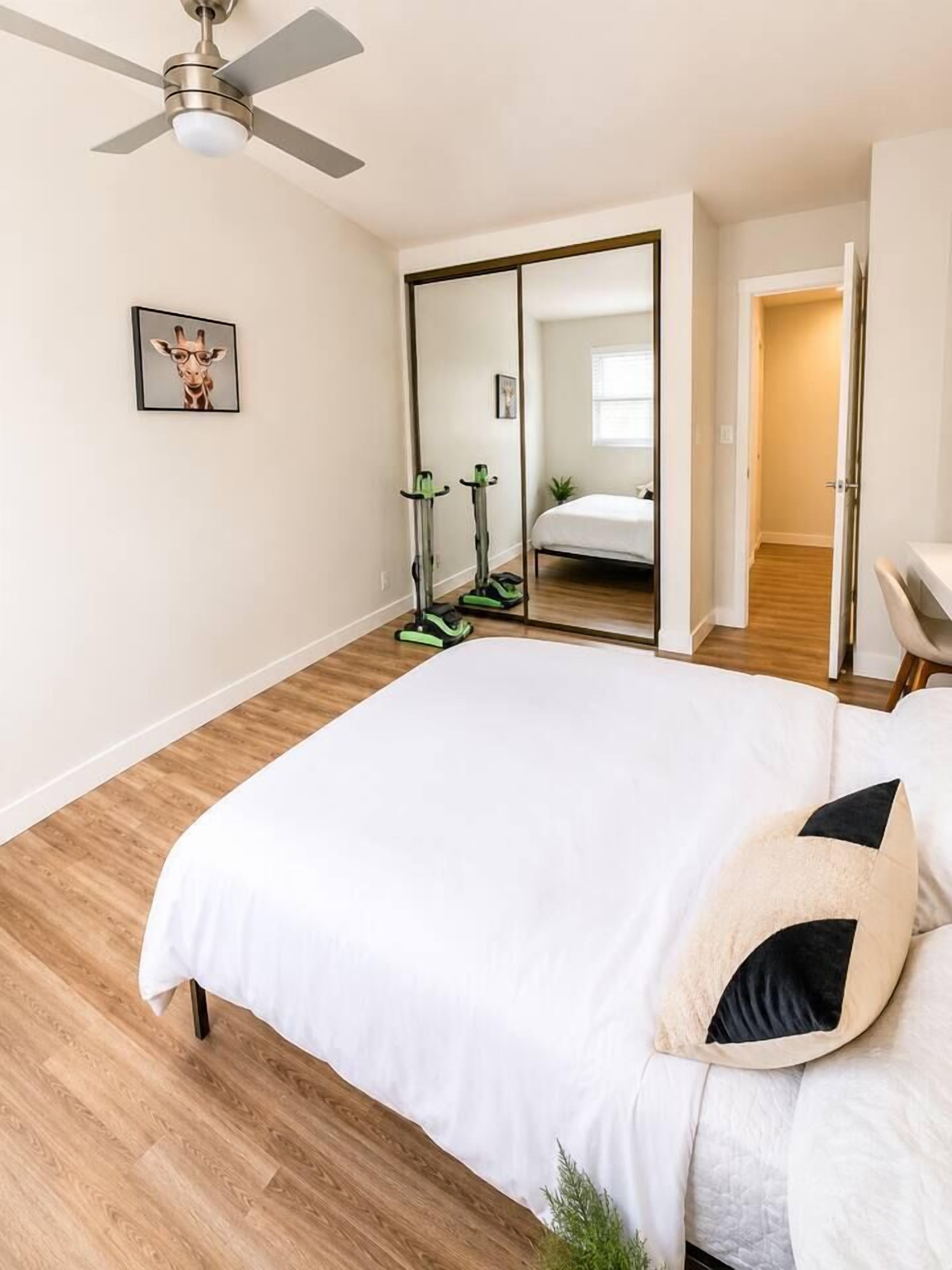 A bedroom with a large bed, a ceiling fan, a mirror, and exercise equipment.