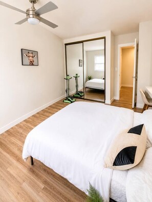 Un dormitorio con una cama grande, ventilador de techo, espejo y equipo de ejercicio.