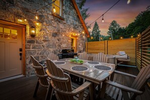 An outdoor patio with a stone wall, wooden furniture, and string lights. - The Banner Elk Collection | 3 Units | Sleeps 12 (Banner Elk)