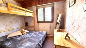 Ein Zimmer mit einem Etagenbett, einem Schreibtisch mit Stuhl, einer Heizung und einem Fenster mit Blick auf Bäume.