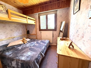 Ein Zimmer mit einem Etagenbett, einem Schreibtisch mit Stuhl, einer Heizung und einem Fenster mit Blick auf Bäume.