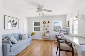 A room with a blue sofa, a wooden chair, a white desk, a bookshelf, and a ceiling fan. - Newly renovated 3BR/2BA coastal beach retreat-sweeping harbor & ocean views. (Scituate)