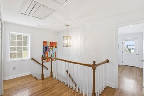 Un escalier avec des rampes en bois et des balustrades blanches, un luminaire au plafond et un tableau accroché au mur.