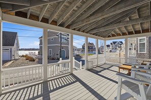 A covered porch with a view of residential buildings, wooden railings, and a bench. - Newly renovated 3BR/2BA coastal beach retreat-sweeping harbor & ocean views. (Scituate)
