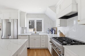 A modern kitchen with white cabinetry, a marble countertop, a gas stove, and a window with blinds. - Newly renovated 3BR/2BA coastal beach retreat-sweeping harbor & ocean views. (Scituate)