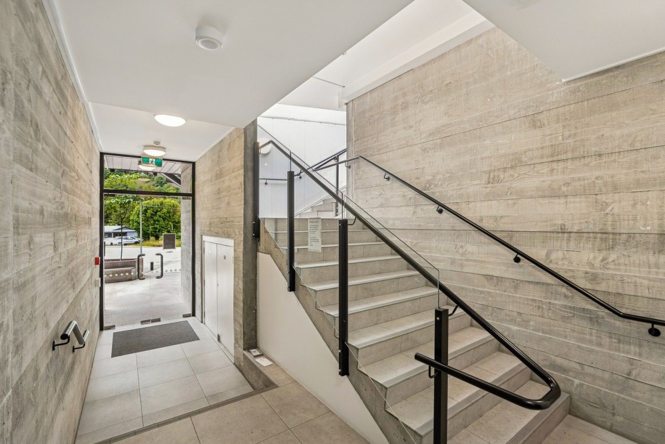 A modern interior with a staircase, a glass door leading outside, and a concrete wall.