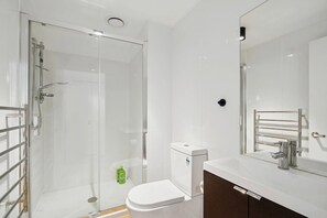 Un baño moderno con cabina de ducha de vidrio, inodoro blanco, lavamanos con espejo y toallero.