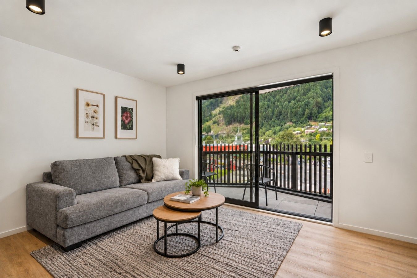 Un salon moderne avec un canapé gris, une table basse ronde et une vue sur un paysage verdoyant, visible à travers de grandes portes-fenêtres coulissantes.