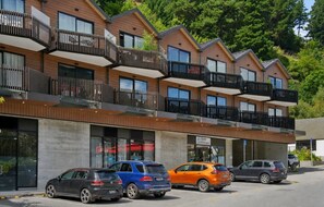 Un edificio de varios pisos con balcones, una fachada visible y automóviles estacionados.