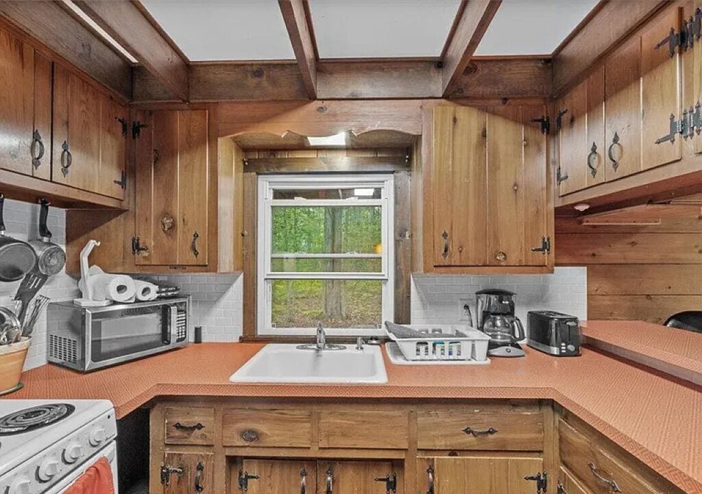 Une cuisine avec des meubles en bois, un évier blanc, une cuisinière et une fenêtre donnant sur un paysage verdoyant.