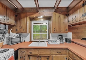 A kitchen with wooden cabinets, a white sink, a stove, and a window with a view of greenery.