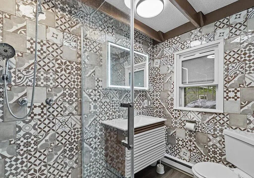 Une salle de bain avec des carreaux décorés, une douche en verre, un lavabo avec un miroir et des toilettes.