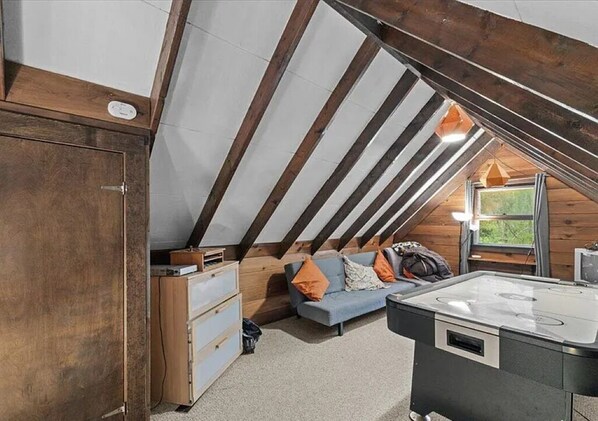 A loft bedroom with a sloped ceiling, a sofa, a small table, and a heater.