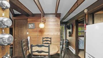 Un intérieur en bois avec une table et des chaises, un luminaire suspendu et un réfrigérateur blanc.