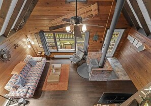A cozy cabin interior with a sofa, chairs, a fireplace, and a large window.